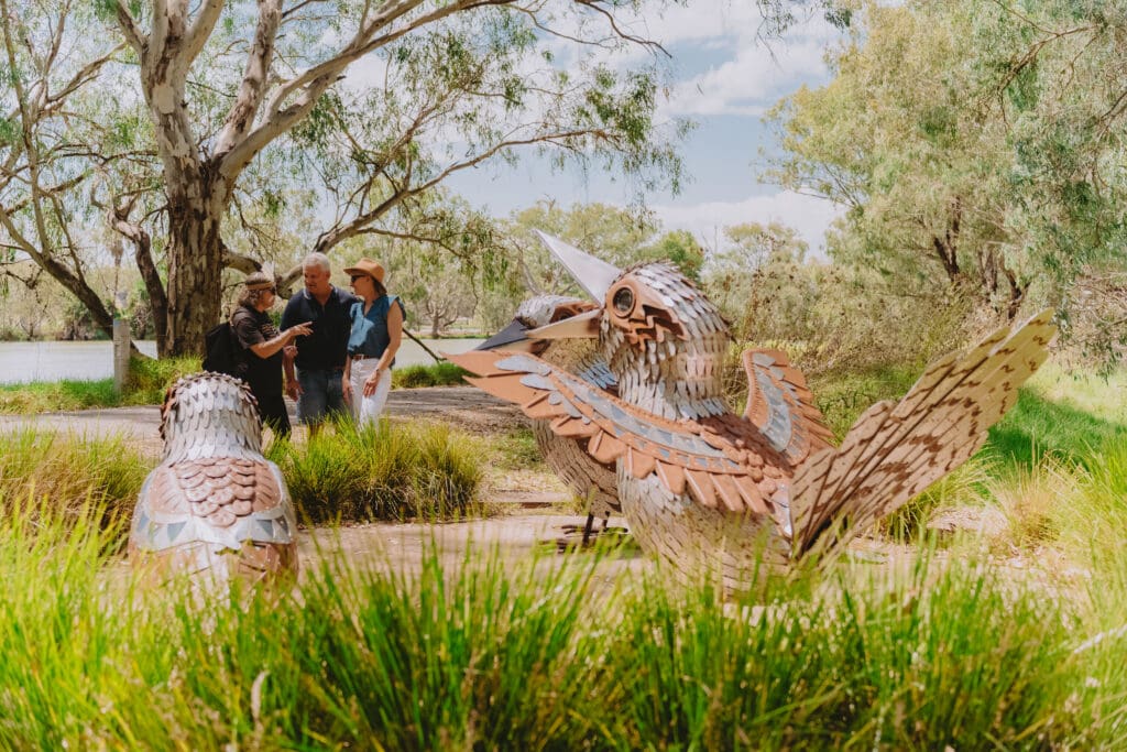 Three people stand close to the 'Guguburras' sculptural piece on the Yindyamarra Sculpture Walk.
