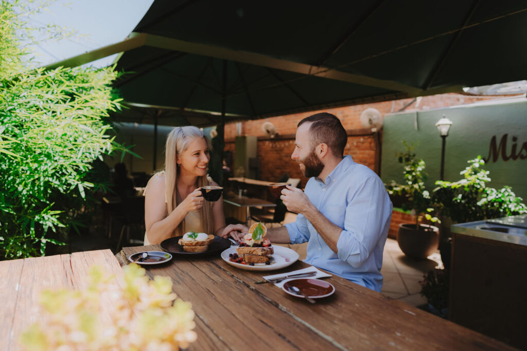 A woman with blonde hair and a man in a blue shirt eat brunch at outdoor cafe table