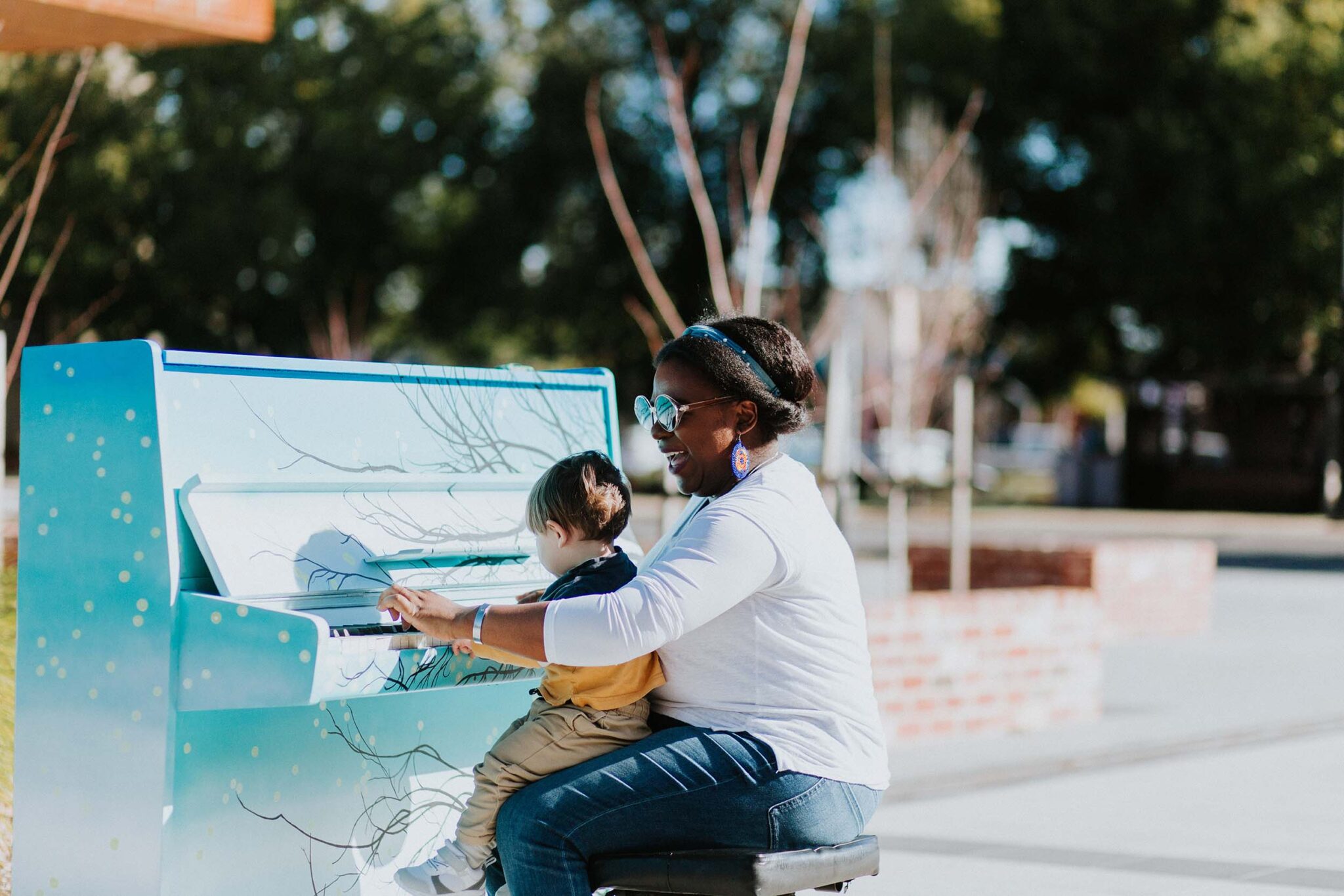 Woman plays public piano with small boy on her lap