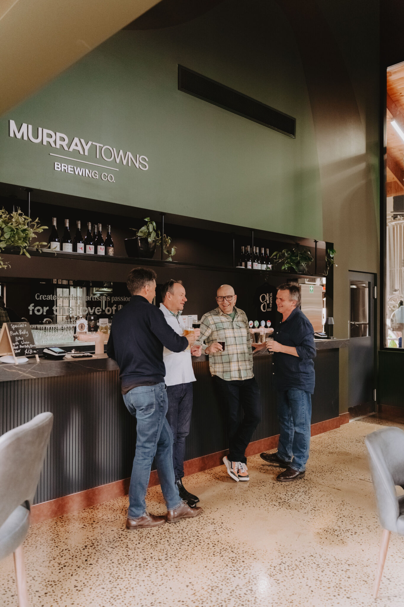 4 men standing in front of bar at brewery drinking beer