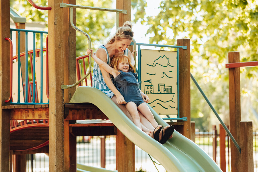 A mum and daughter sliding down a slide in a park