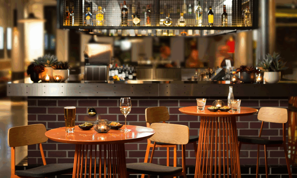 Hotel bar with modern orange tables set with drinks and bar snacks.
