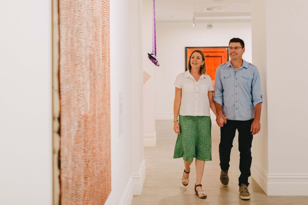Smiling couple walking hand in hand through an art gallery, viewing colorful and contemporary artworks on white walls