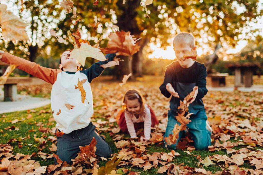 Three children play in autumn leaves in Noreuil Park at golden hour.