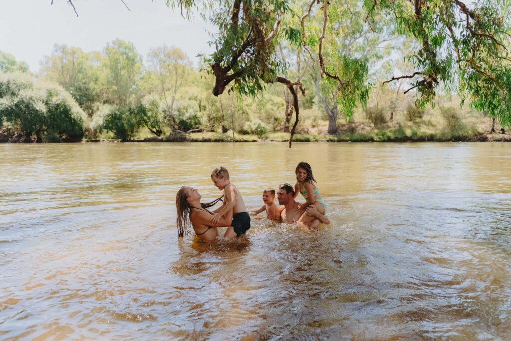 Family plays in the river under the shade of a gum tree