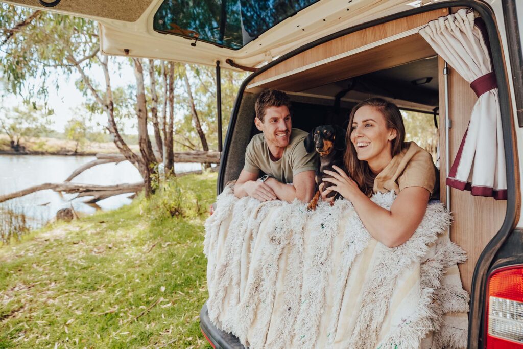 Couple relaxing with their small dog inside a cozy campervan parked under shady trees in Albury Wodonga.