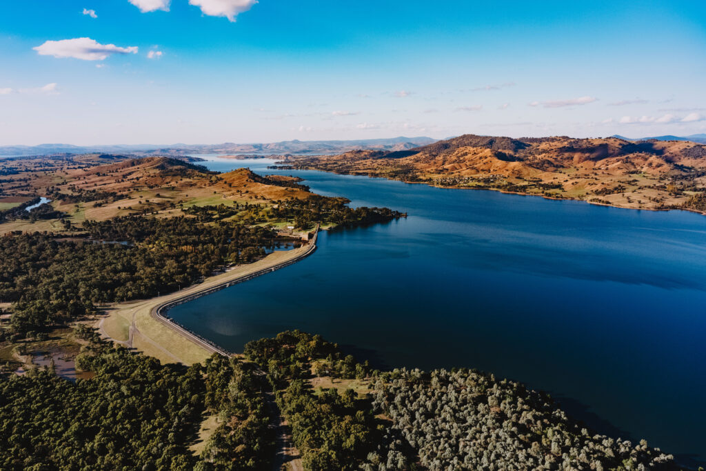An ariel image over blue water to the right and trees and hills to the left.
