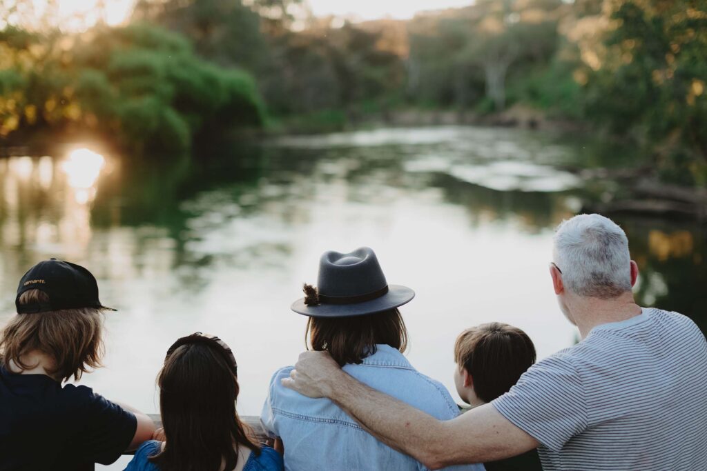 A family of five look out over the Murray River at sunset, with leafy green trees in the background