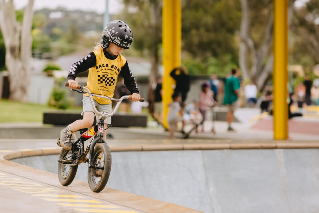 A young boy in a black and yellow long sleeve t-shirt is riding is bmx bike at a skate park