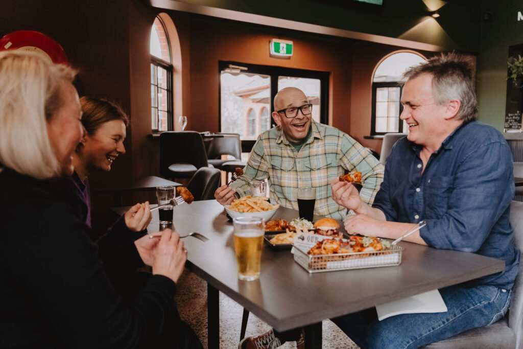 A group of four people laughing, eating and drinking beers