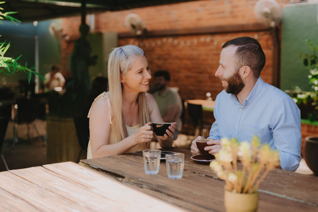 A blonde woman wearing a beige top and a man with a blue shirt drinking coffee