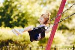 Young girl with a big smile buckled into toddler swing, captured at the top of the swing's arc